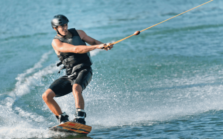 A person wakeboarding and another waterskiing on a calm lake, with a boat pulling them in opposite directions