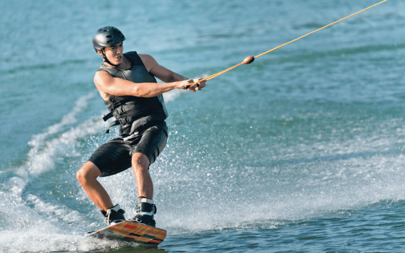 A person wakeboarding and another waterskiing on a calm lake, with a boat pulling them in opposite directions